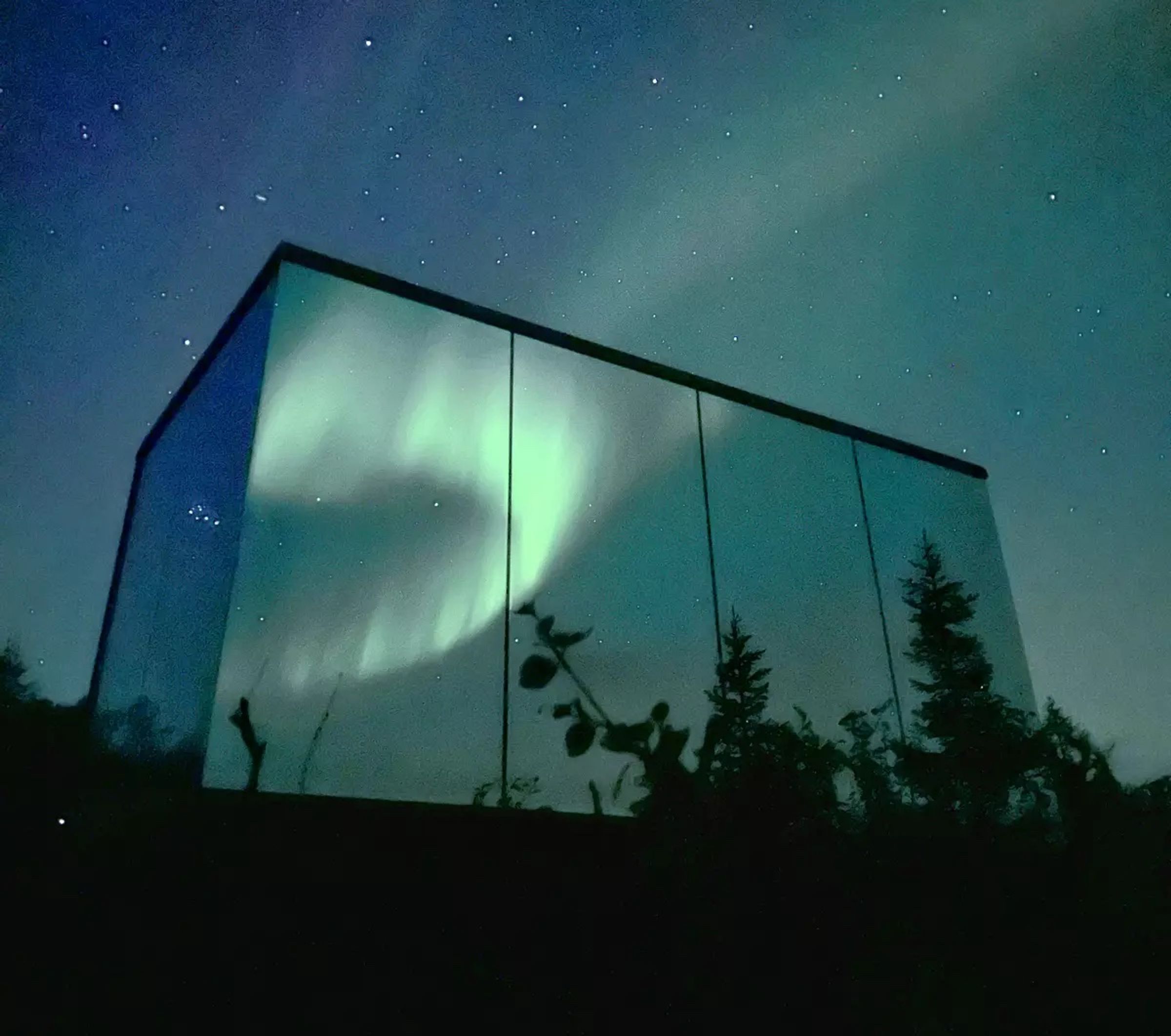 Northern lights reflected in the glass of a mirror cabin in Northern Norway