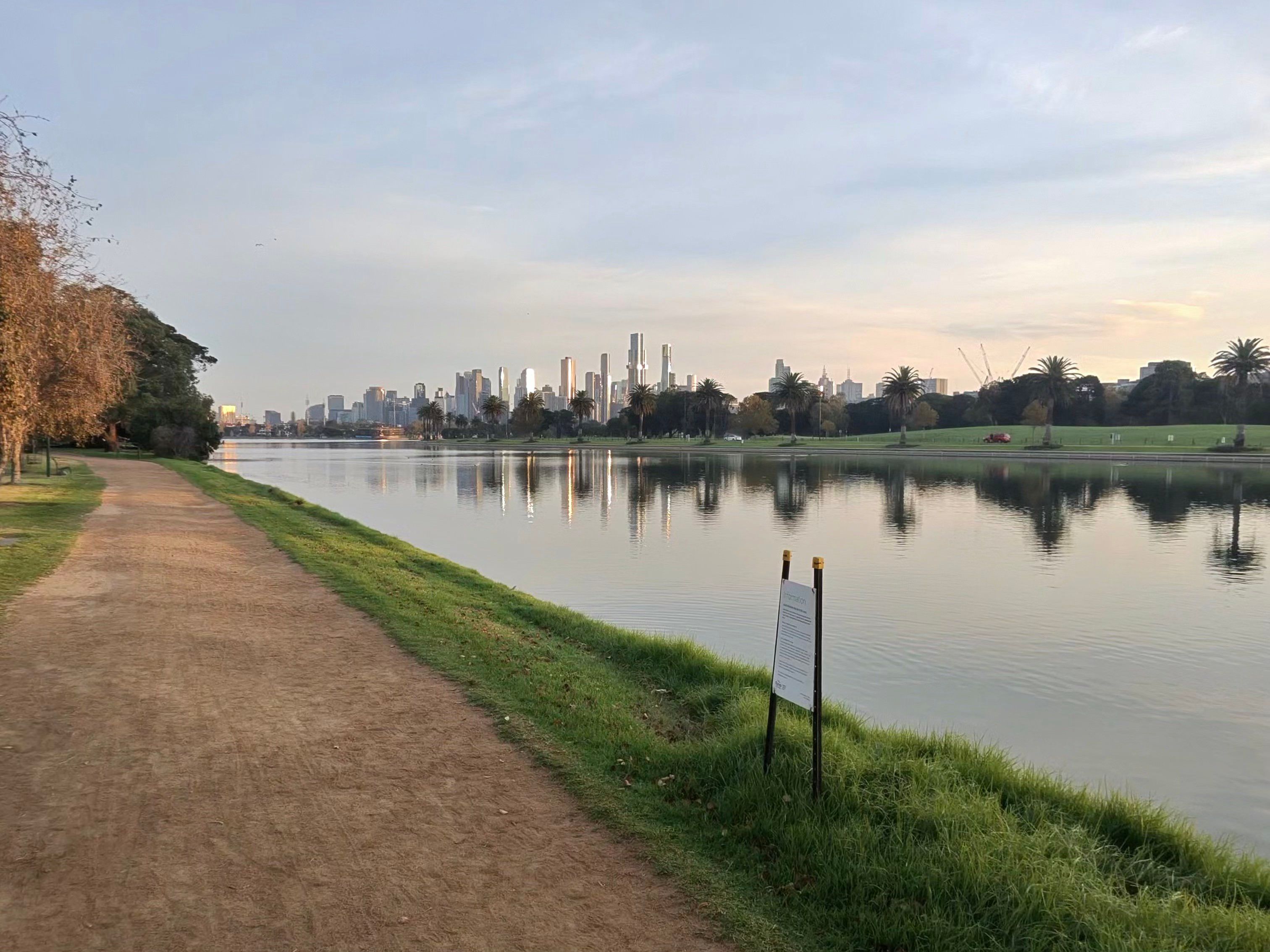 Albert Park Lake at sunrise, the path along the bank and the Melbourne skyline beyond.
