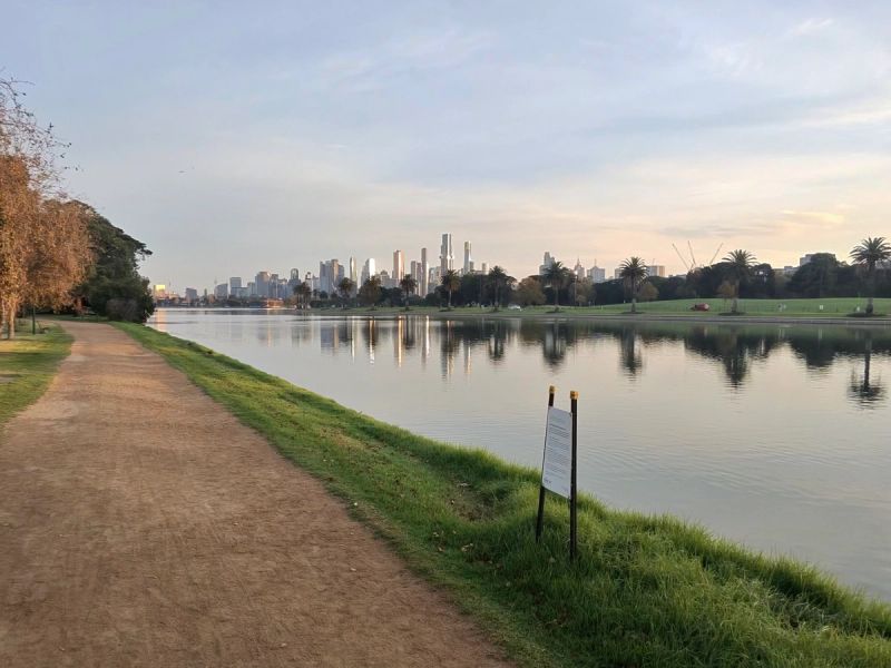 Albert Park Lake at sunrise, the path along the bank and the Melbourne skyline beyond.