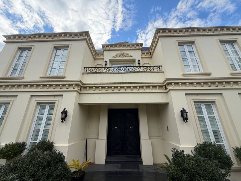 Beige rendered two-storey house on South Road with black doors and an iron balcony rail