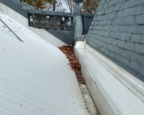 Box gutter behind a parapet on a Middle Park terrace with dried leaves banked along the roof join