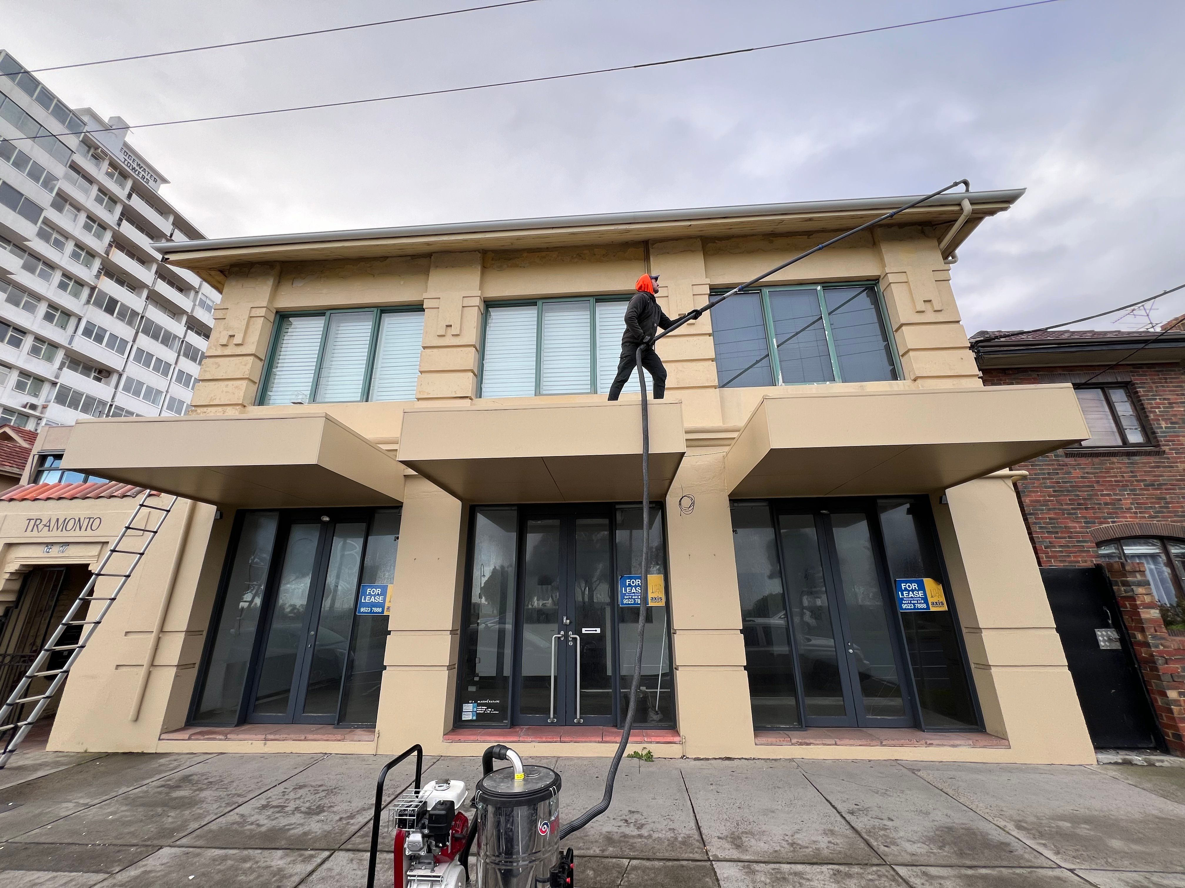 Technician clearing the gutter of a rendered interwar building in St Kilda with a vacuum pole