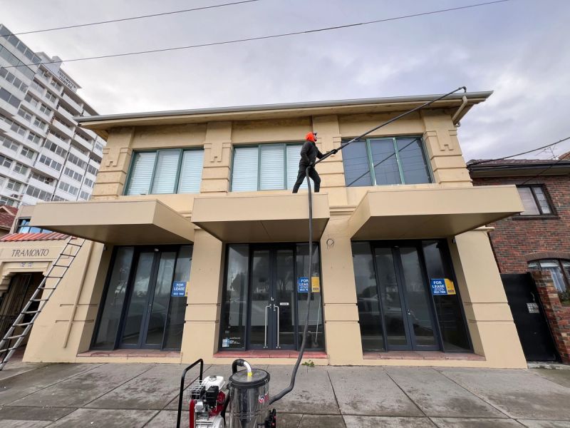 Technician clearing the gutter of a rendered interwar building in St Kilda with a vacuum pole