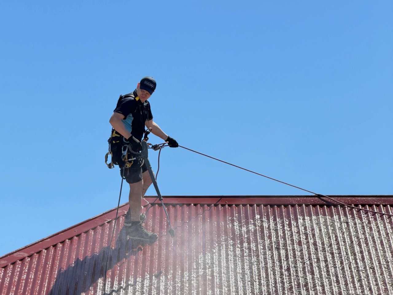 WaterCrew technician on rope access soft-washing a Colorbond roof in Melbourne