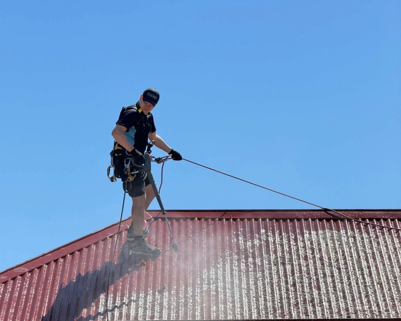 WaterCrew technician on rope access soft-washing a Colorbond roof in Melbourne