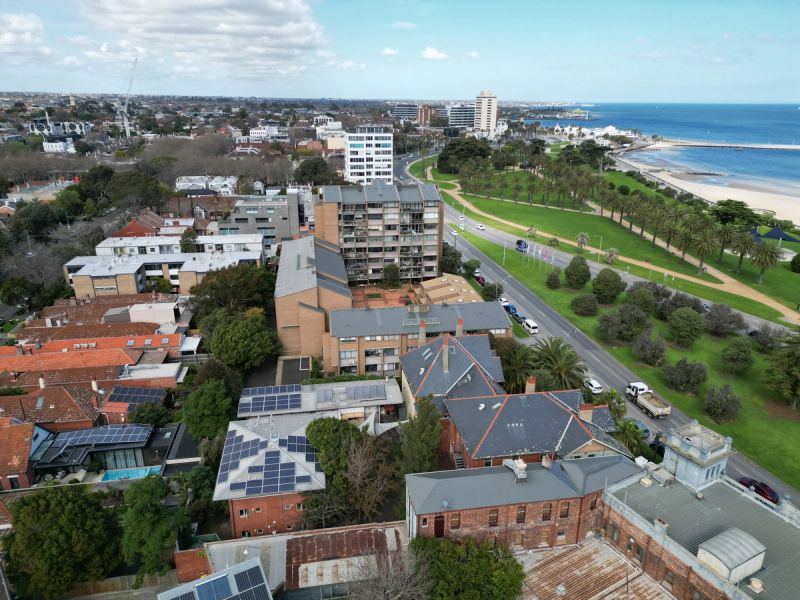 Aerial view over St Kilda West rooftops towards Beaconsfield Parade, the foreshore palms and Port Phillip Bay.
