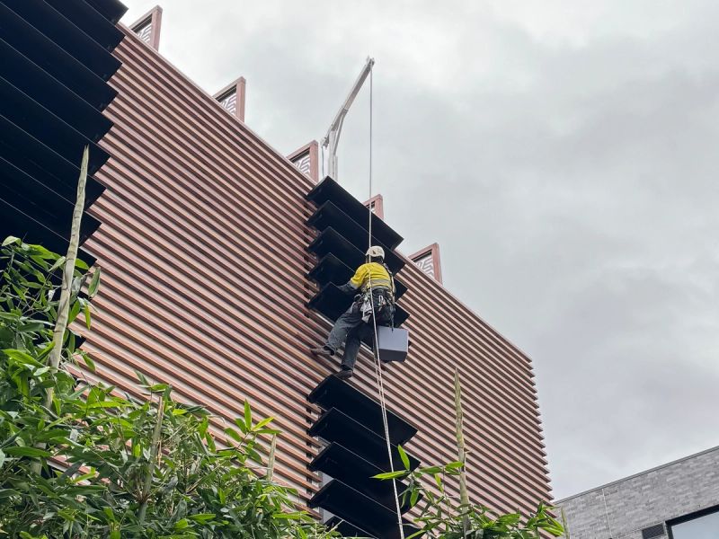 Rope access technician cleaning a modern battened facade on a St Kilda building