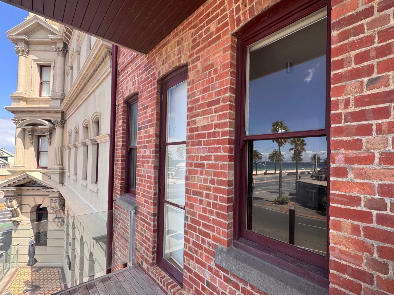 Windows set beyond the balcony of a red-brick apartment on Beaconsfield Parade, looking out to the palms and Albert Park Beach