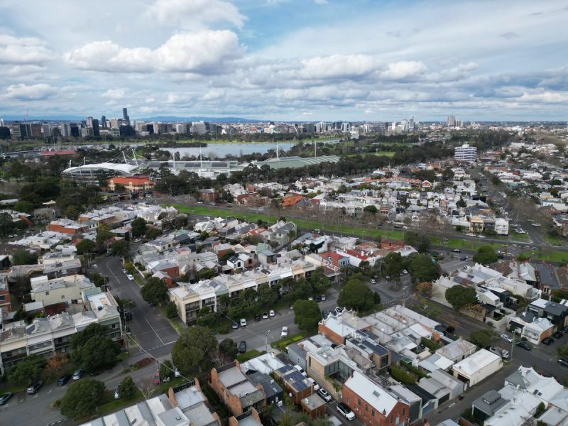 Aerial view over Albert Park rooftops towards Albert Park Lake and the Melbourne city skyline.