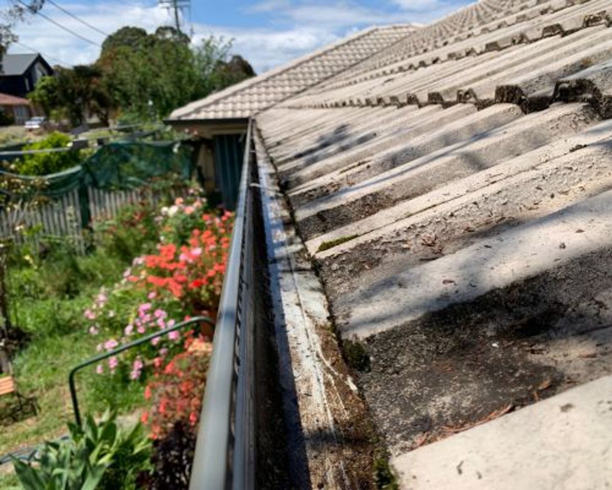 The same gutter cleared back to bare metal, with moss still visible on the concrete tiles above