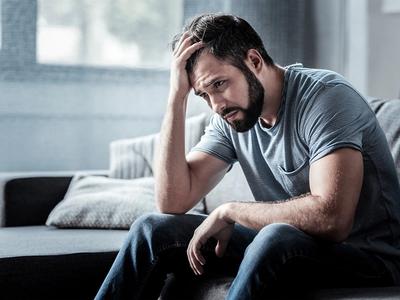 Man sitting on couch with head in hand - representing emotional exhaustion, low mood, and recovery through functional medicine treatment for depression in Denver, Colorado Springs, and Fort Collins