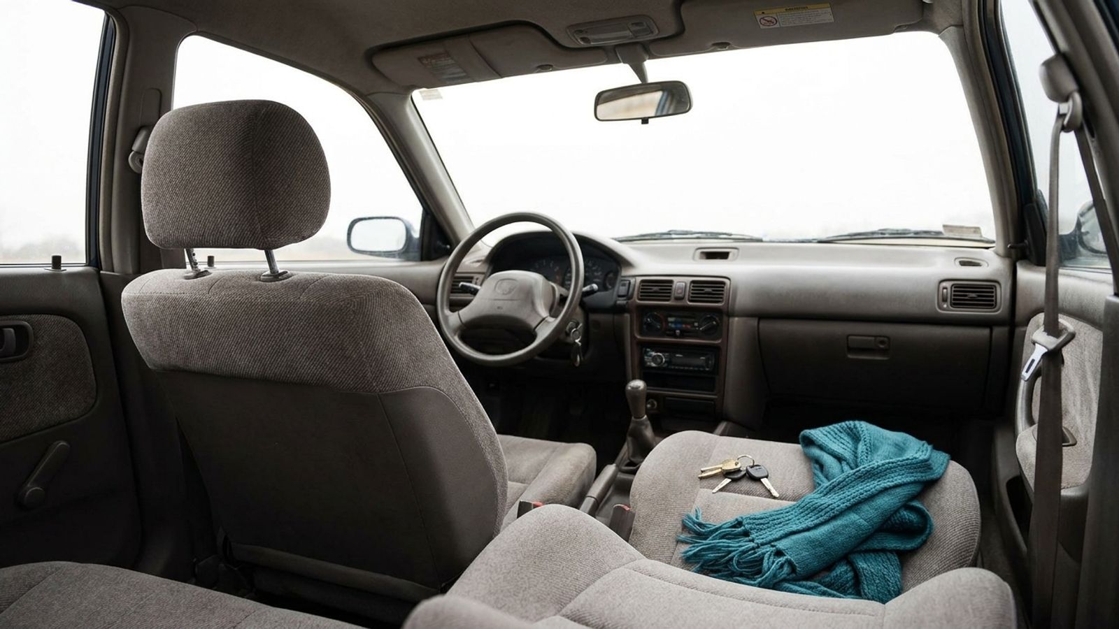The empty front seats of a car, with keys and a teal scarf on the passenger seat