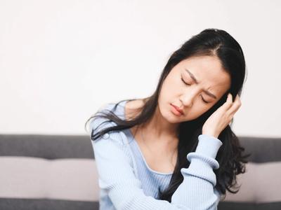 Woman sitting on couch holding her head and neck in discomfort - representing lingering fatigue, inflammation, and recovery support through functional medicine treatment for post-viral syndromes including Long COVID and post-infectious conditions in Denver, Colorado Springs, and Fort Collins