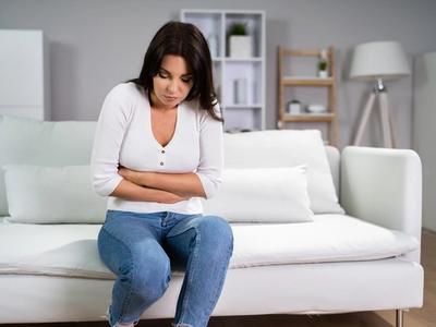 Woman sitting on couch holding her stomach - representing abdominal discomfort, bloating, and digestive inflammation improved through functional medicine treatment for diverticulitis in Denver, Colorado Springs, and Fort Collins