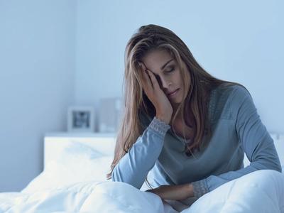Woman sitting in bed looking tired and restless - representing sleep disturbances, nighttime anxiety, and hormone imbalance improved through functional medicine treatment for insomnia in Denver, Colorado Springs, and Fort Collins