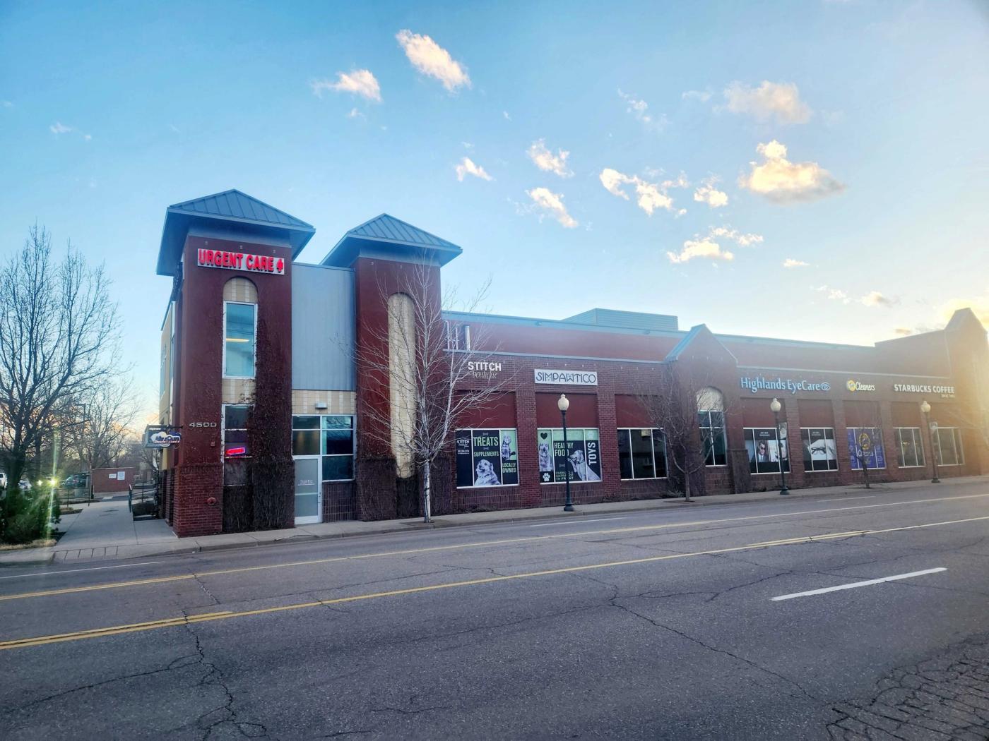 AfterOurs Urgent Care in Denver Highlands: a red brick corner building with illuminated Urgent Care signs at dusk