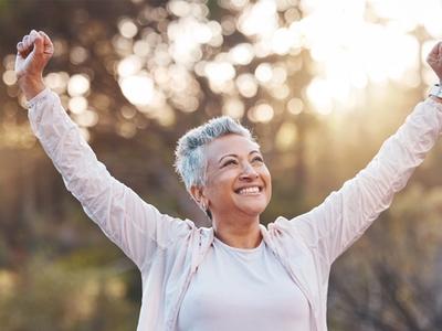 Smiling woman outdoors raising her arms in victory - representing reduced inflammation, improved circulation, and relief from fluid retention through functional medicine treatment for swelling in Denver, Colorado Springs, and Fort Collins