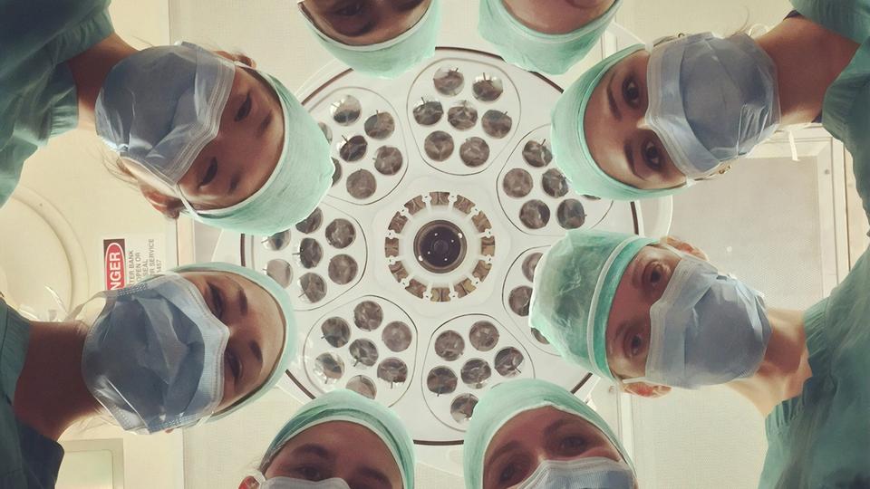 Team of doctors in surgical masks looking down under operating room light ΓÇö representing clinical expertise, collaboration, and the expansion of Spire Health PathwaysΓÇÖ functional medicine team with the addition of two new MDs and DOs serving patients in Denver, Colorado Springs, and Fort Collins