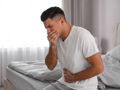 Man sitting on bed holding his stomach and covering mouth - representing nausea, digestive distress, and gut-brain imbalance relieved through functional medicine treatment for nausea in Denver, Colorado Springs, and Fort Collins