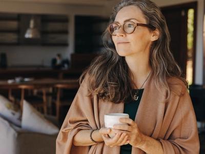 Calm middle-aged woman holding a warm drink and looking out the window - representing nerve health, circulation support, and recovery from unexplained numbness and tingling through functional medicine treatment in Denver, Colorado Springs, and Fort Collins