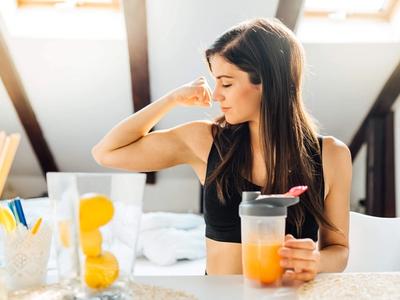 Woman drinking a healthy smoothie and flexing her arm - symbolizing immune strength, reduced inflammation, and recovery through functional medicine treatment for autoimmune and allergic disorders in Denver, Colorado Springs, and Fort Collins