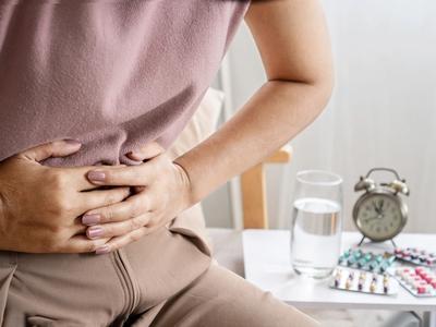 Person holding stomach in pain with medicine and water nearby - representing bloating, cramping, and digestive imbalance relieved through functional medicine treatment for irritable bowel syndrome (IBS) in Denver, Colorado Springs, and Fort Collins