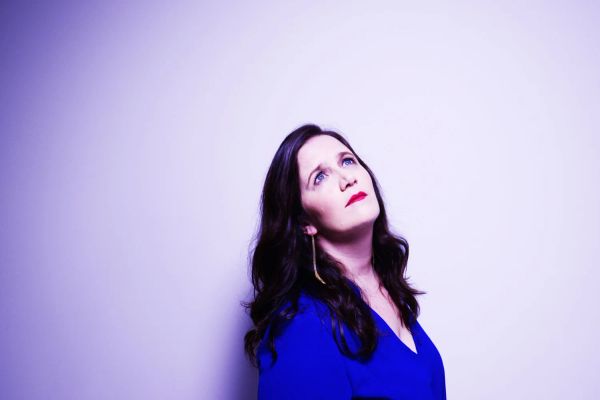 Amy Cervini in a blue dress against a violet backdrop, hi-res press photo