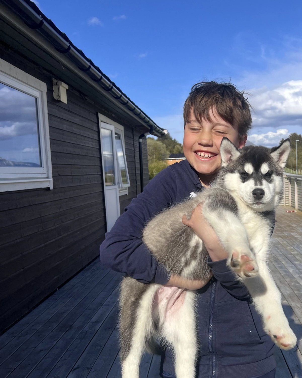 Sønnen i familien Tornes løfter opp Boo på verandaen i sola.