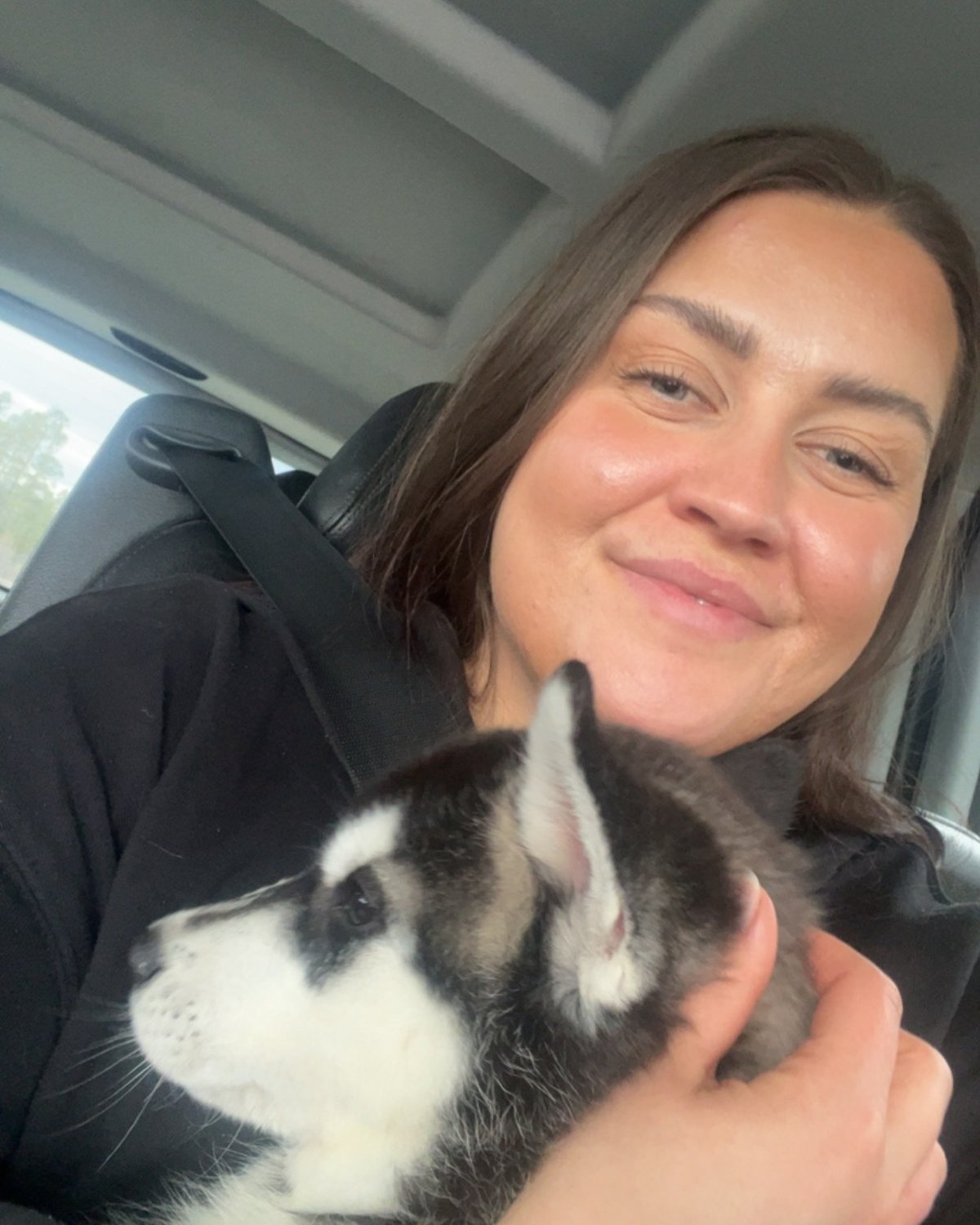 Mathilde sitter i bilen med Boo, en ni uker gammel svart-hvit siberian husky-valp i armene.