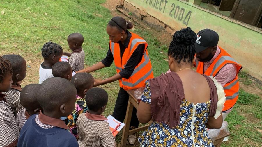 Volunteers handing notebooks to pupils at a table in the schoolyard