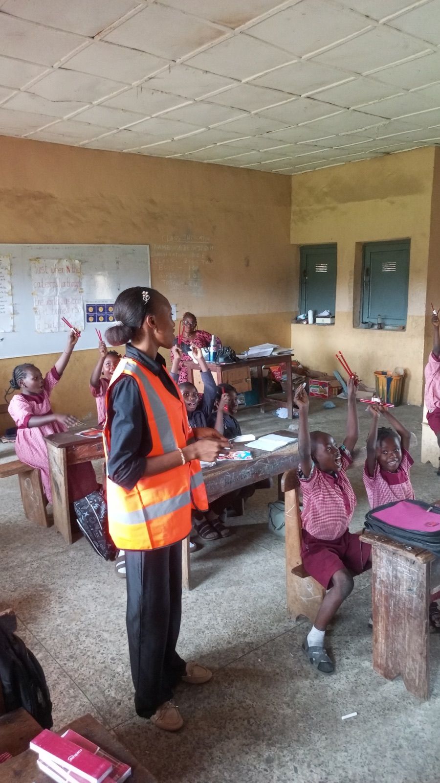A volunteer in a classroom with pupils raising their hands