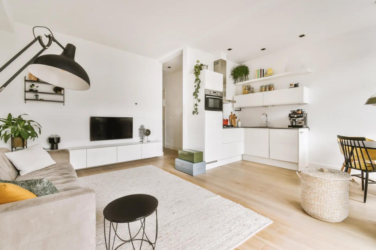 Offene weiße Wohnküche mit Holzboden, davor Wohnzimmer mit Sofa und TV-Lowboard