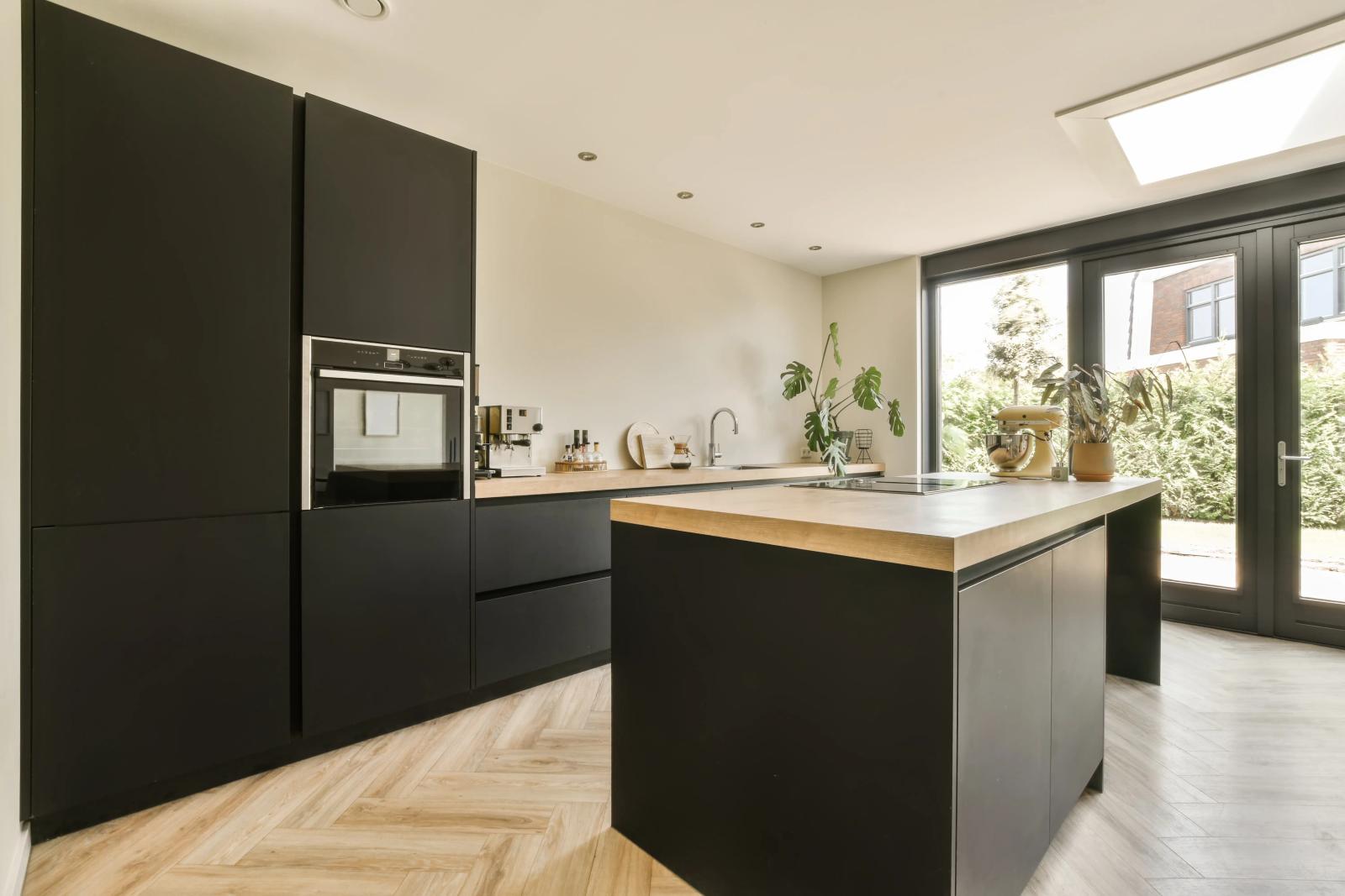 Luxuriöse grifflose Designküche in Schwarz mit Kochinsel, Barhockern und auffälliger Rückwand in Fischgrätmuster.