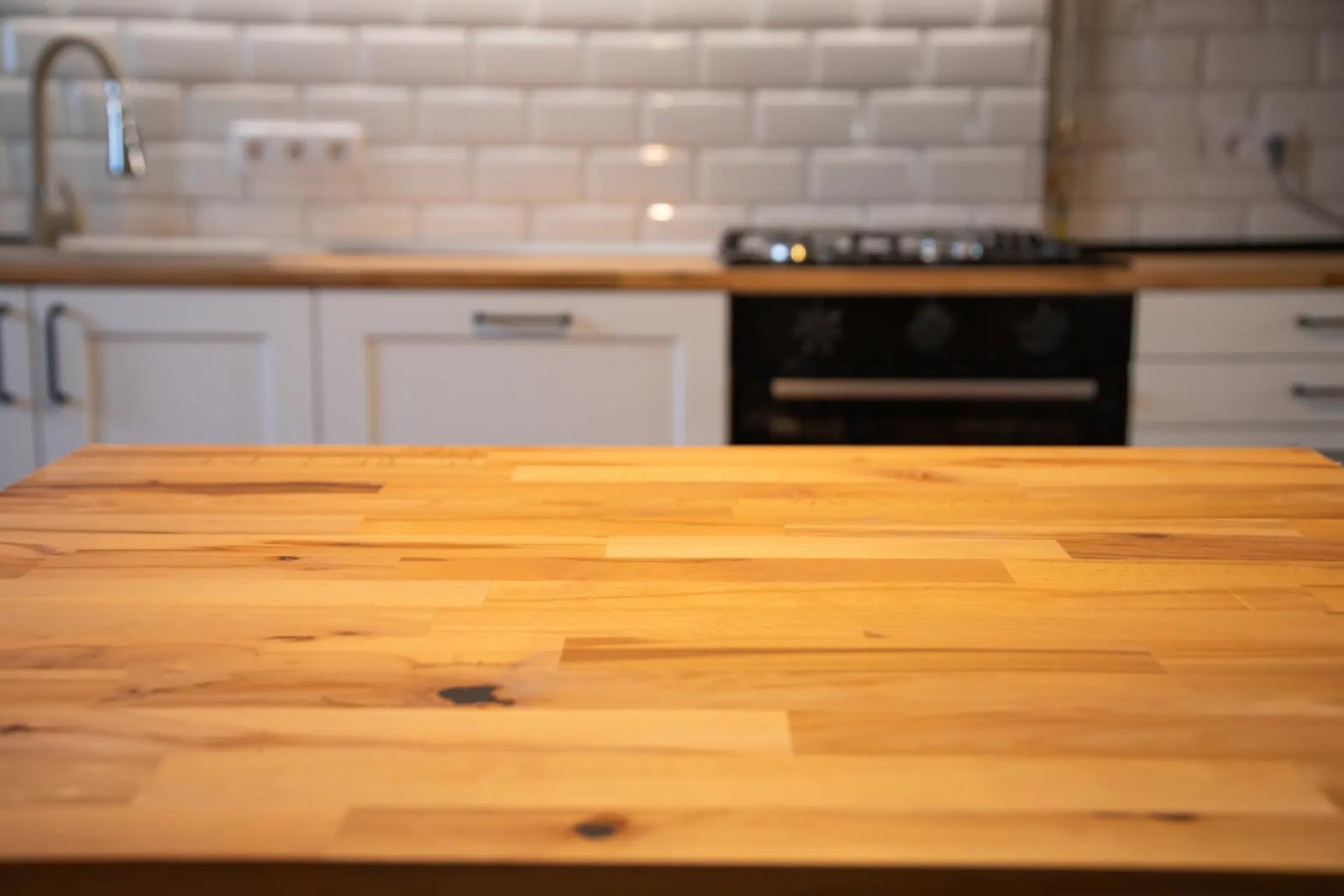 Nahaufnahme einer sauberen Küchenarbeitsplatte aus Holz, im Hintergrund weiße Küchenmöbel und Fliesen, Tipps, wie du deine Küchenarbeitsplatte richtig reinigen kannst.