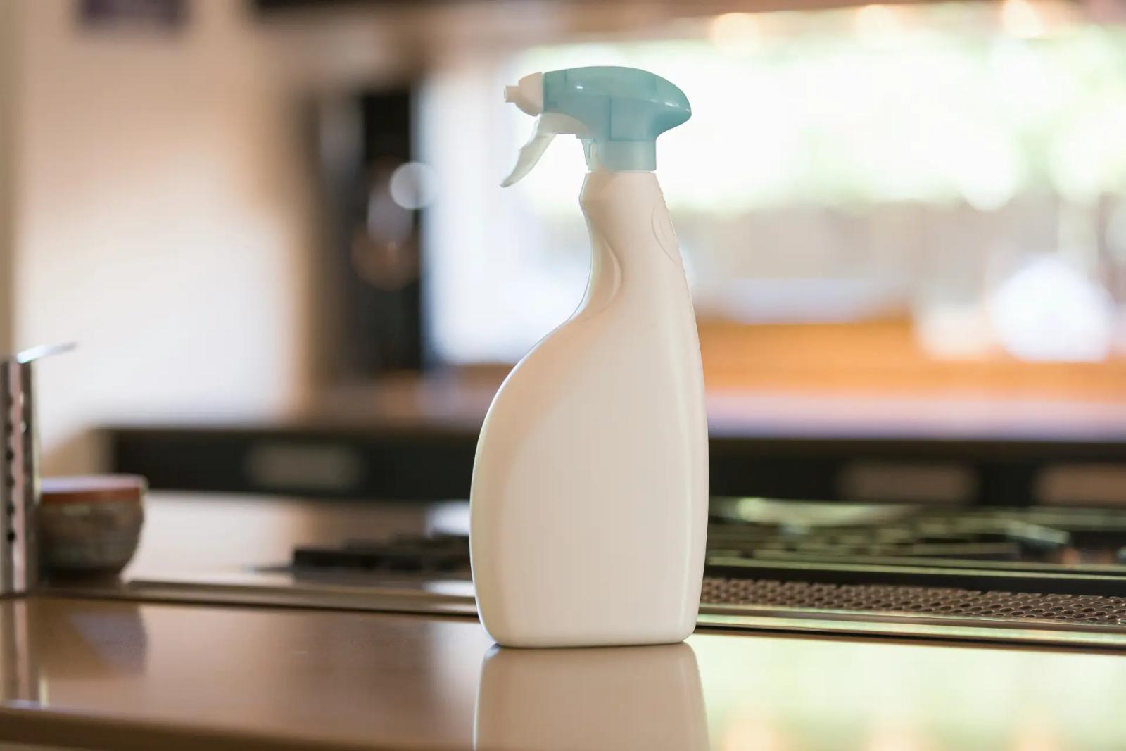 Weiße Sprühflasche mit Reiniger auf der Küchenarbeitsplatte, Küche unscharf im Hintergrund