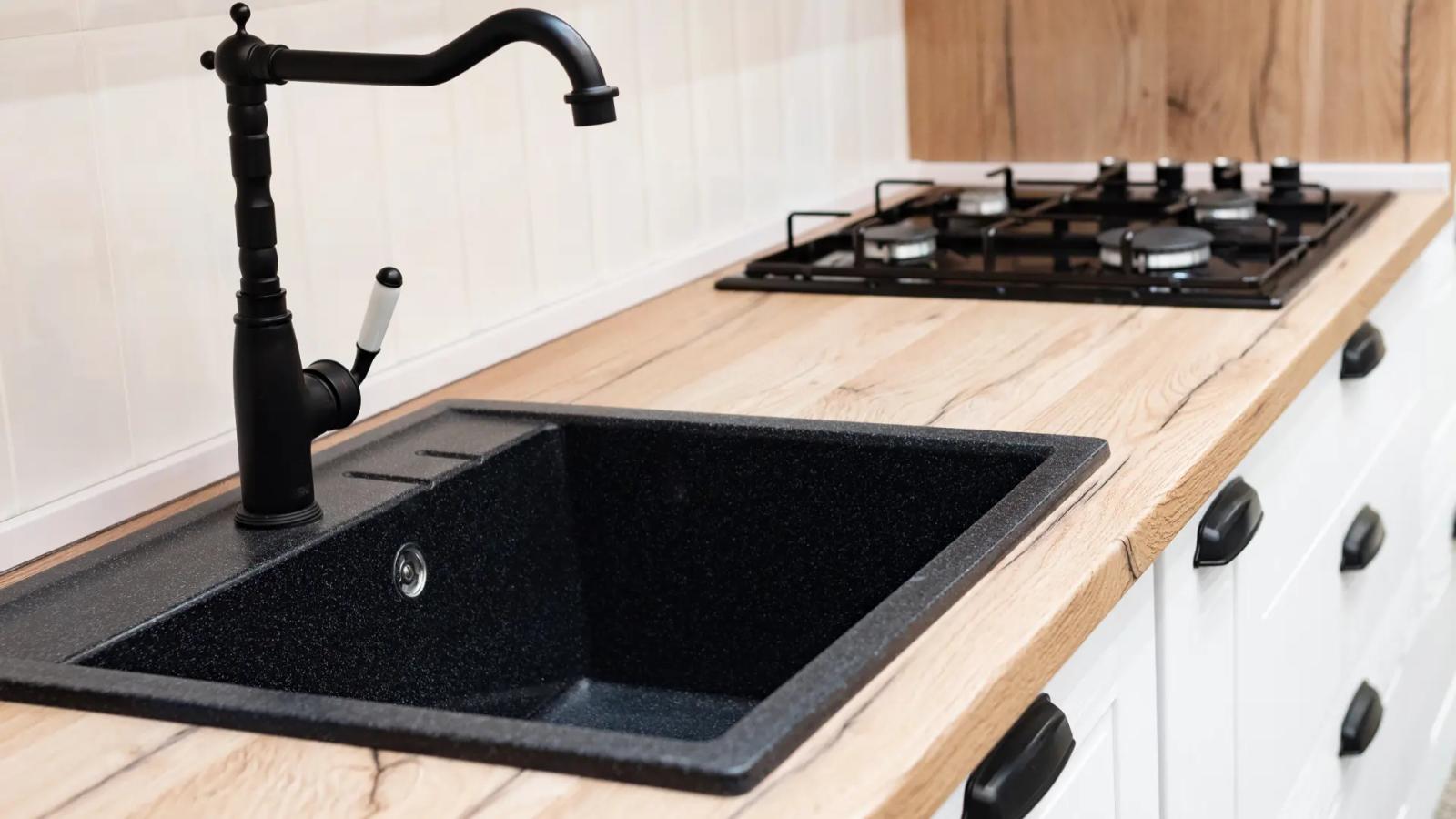 Schwarzes Granitspülbecken mit Retro-Wasserhahn auf heller Holzarbeitsplatte neben einem Gasherd in einer modernen Küche