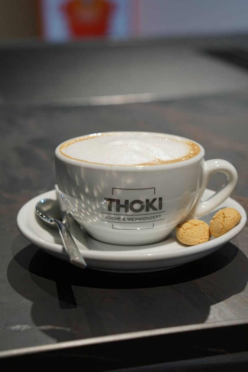 Erstkontakt im Thoki Studio Wörthsee: eine THOKI-Cappuccino-Tasse mit Amaretti auf der dunklen Liveküchen-Theke, einladende Atmosphäre für das erste Gespräch