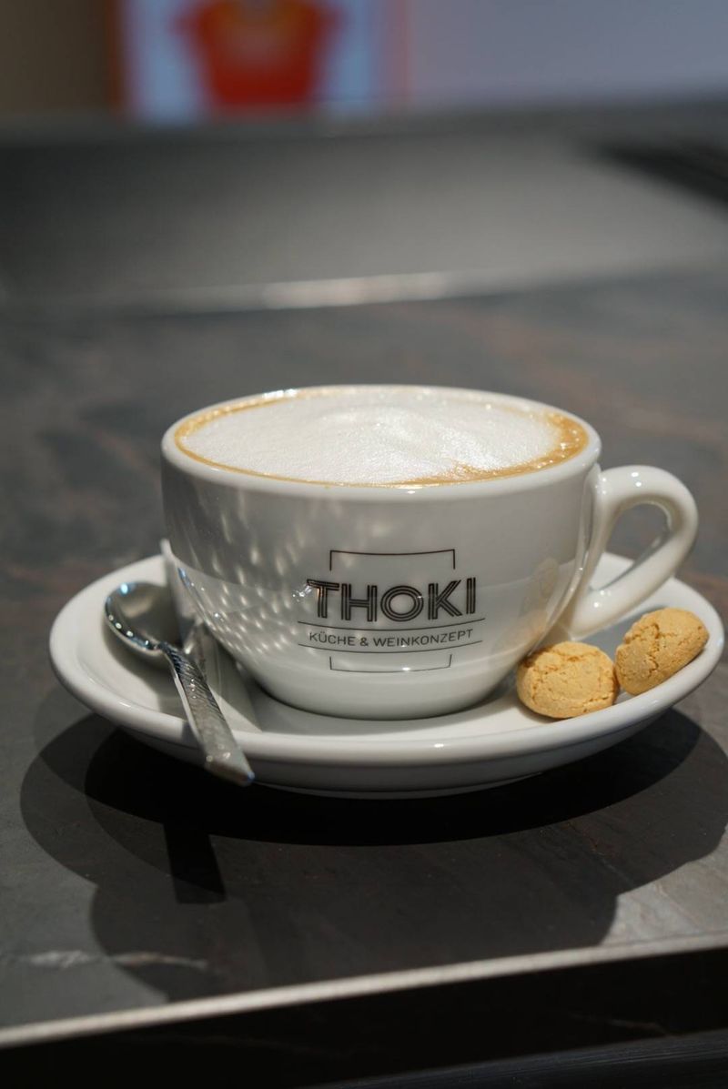 Erstkontakt im Thoki Studio Wörthsee: eine THOKI-Cappuccino-Tasse mit Amaretti auf der dunklen Liveküchen-Theke, einladende Atmosphäre für das erste Gespräch