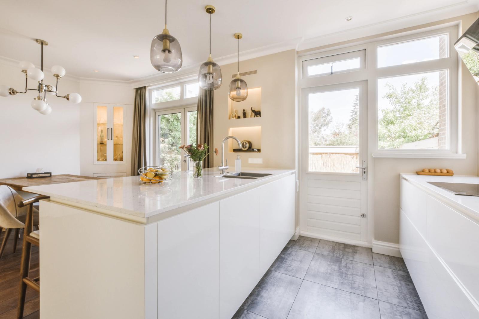Moderne grifflose Küche mit heller Kochinsel, Hängelampen und großem Fensterbereich, gestaltet im minimalistischen Stil.