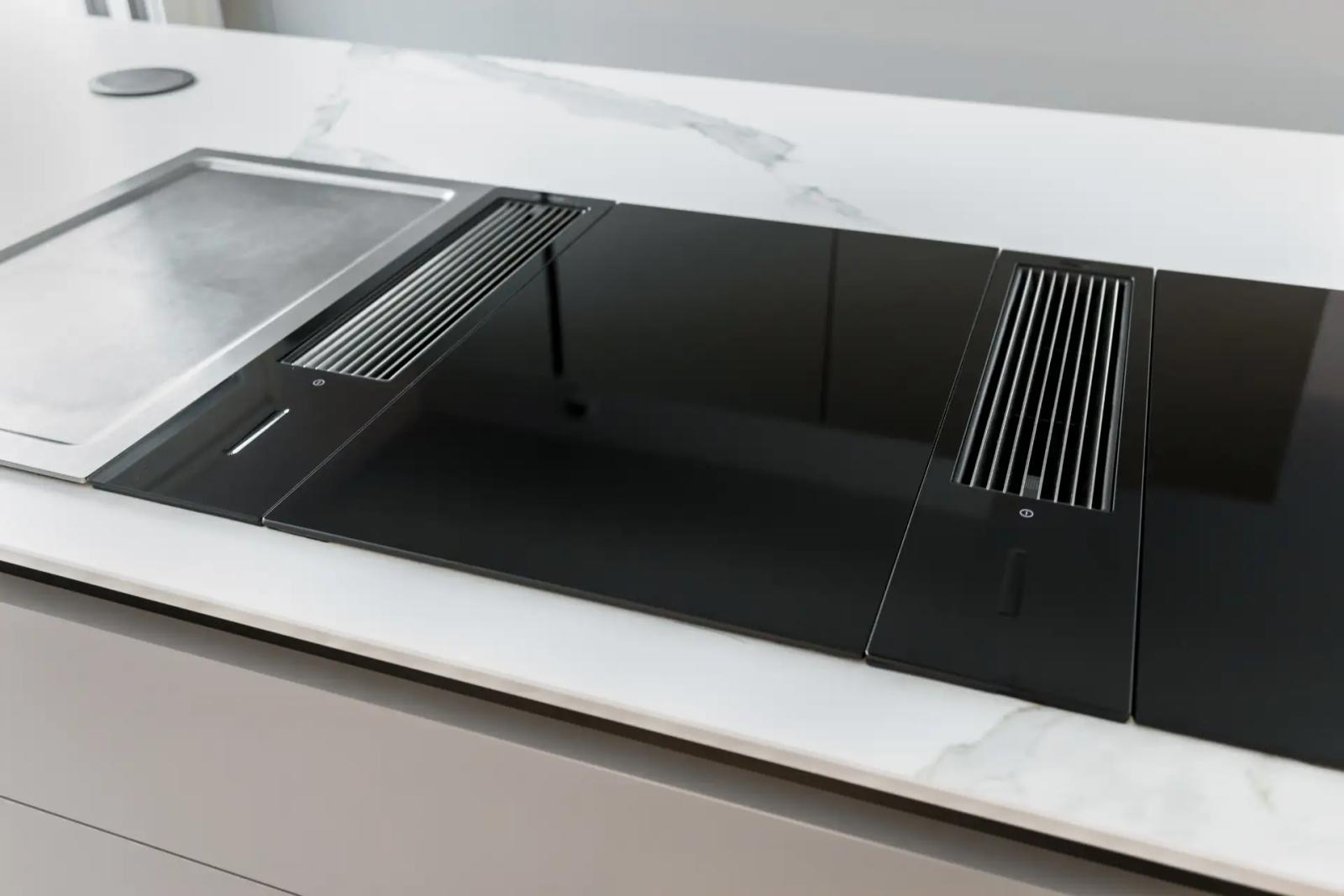 Schwarzes Induktionskochfeld mit zwei Kochfeldabzügen in einer Insel mit weißer Marmor-Optik