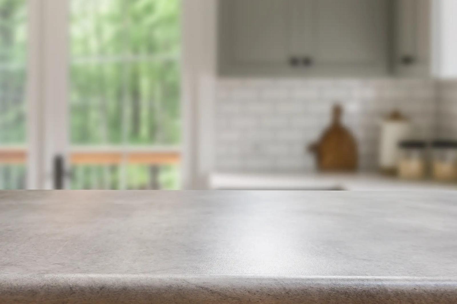 Nahaufnahme einer leeren, sauberen Arbeitsplatte aus grauem Stein mit verschwommener Küche im Hintergrund, Tipps für das richtige Reinigen der Küchenarbeitsplatte.