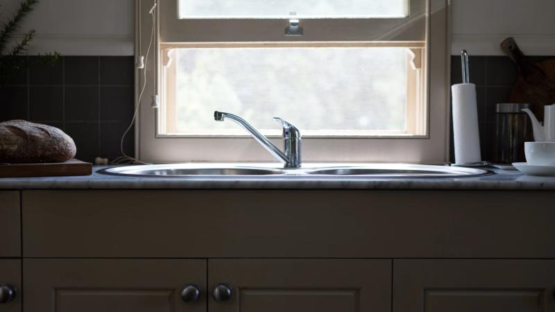 Edelstahlspüle mit Chrom-Armatur in Thoki Küche, natürliches Tageslicht durch Fenster, moderne Arbeitsplatte