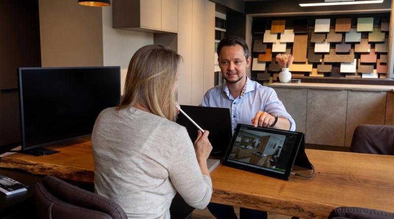 Beratung im Thoki Studio: Thomas zeigt einer Kundin die Küchenplanung am Tablet, Material-Wand im Hintergrund