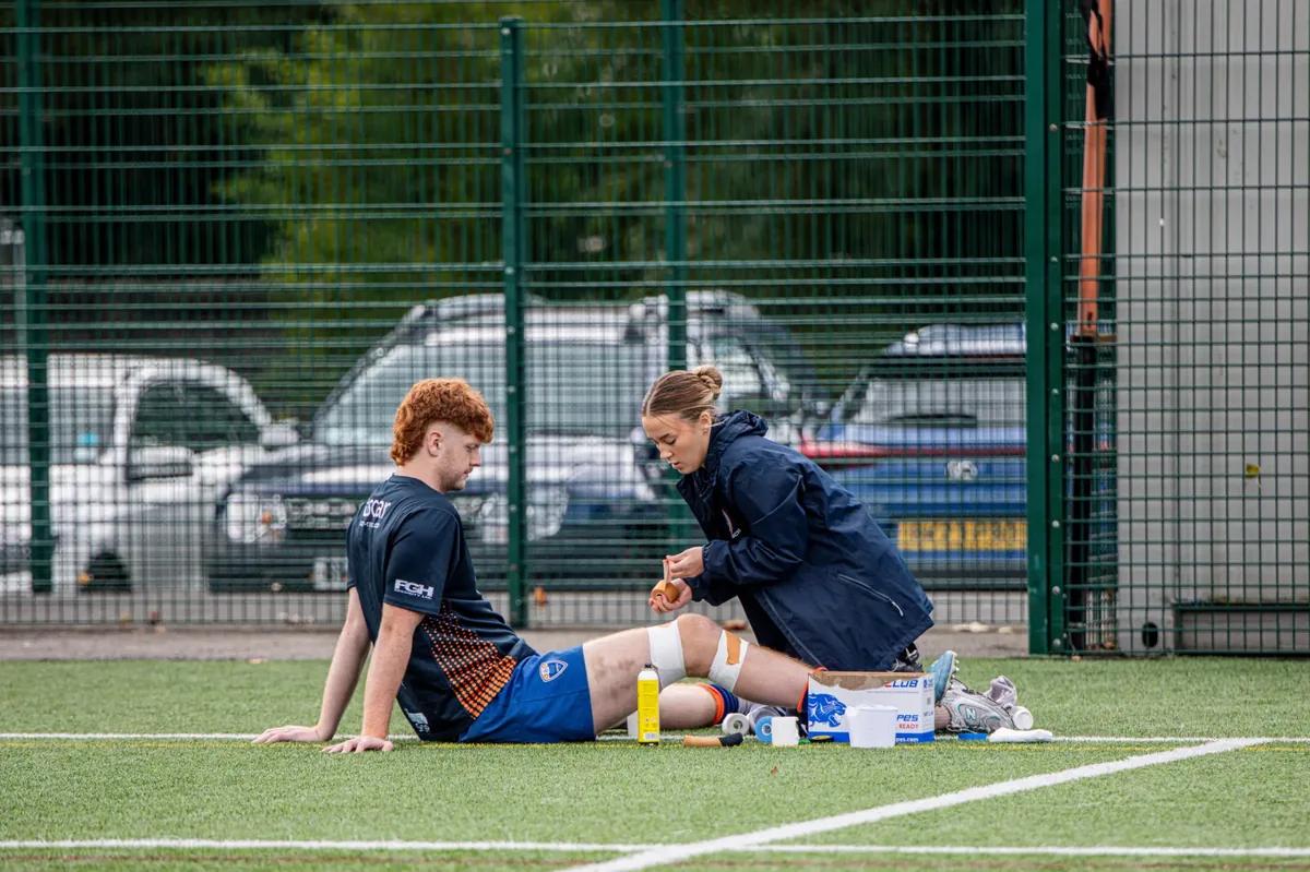 Sports medicine provider taping athlete's knee on pitch — AI athlete management software for injury prevention