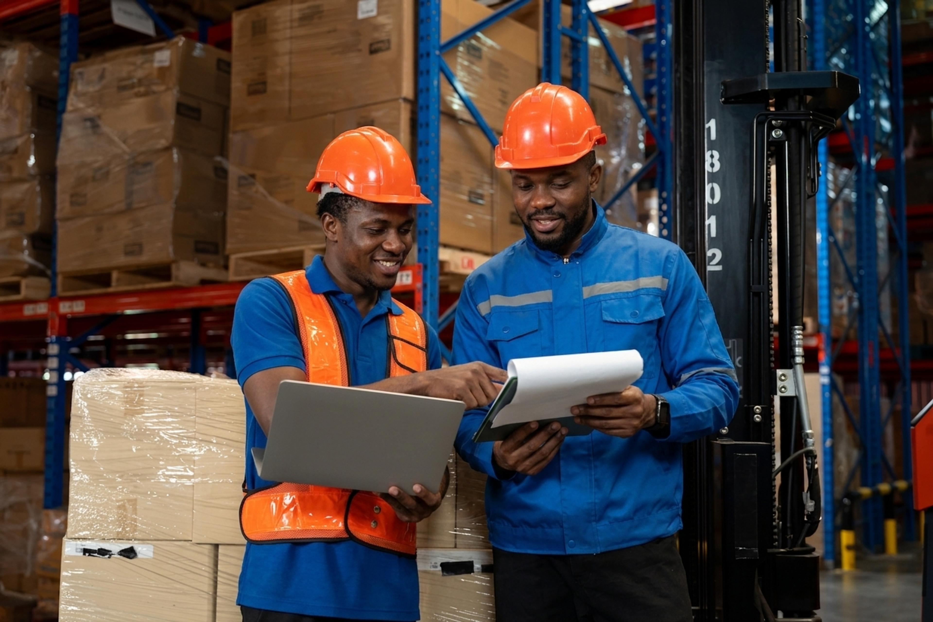 Two specialists in PPE reviewing supplier documentation in a warehouse