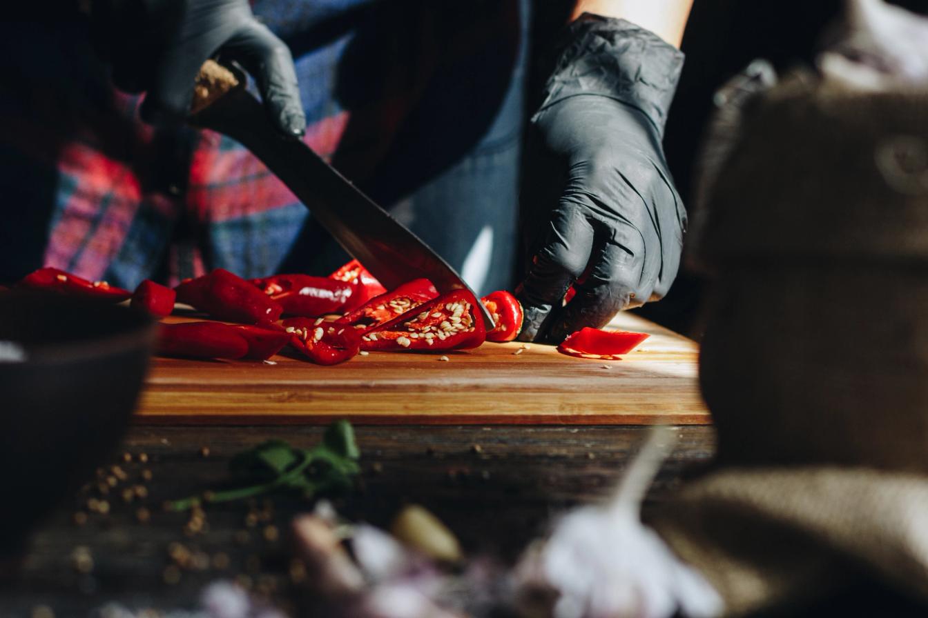 Frau schneidet Chilis mit Handschuhen