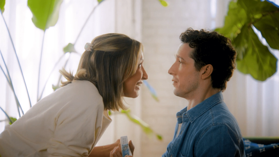 Two actors face each other in a bright room in a still from Viva Media's Book Outlet commercial.