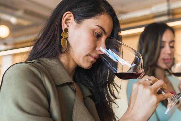 Eine Frau riecht bei einer Verkostung an einem Glas Rotwein, im Hintergrund eine weitere Besucherin