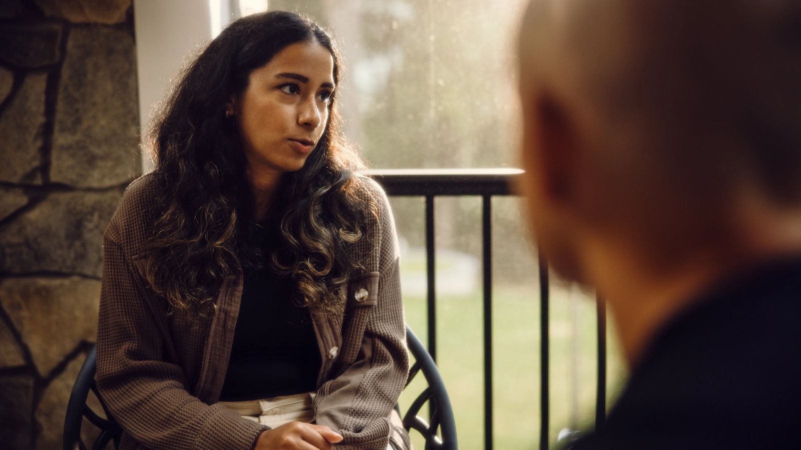 A young woman sits listening intently during a conversation with an older person on a porch.