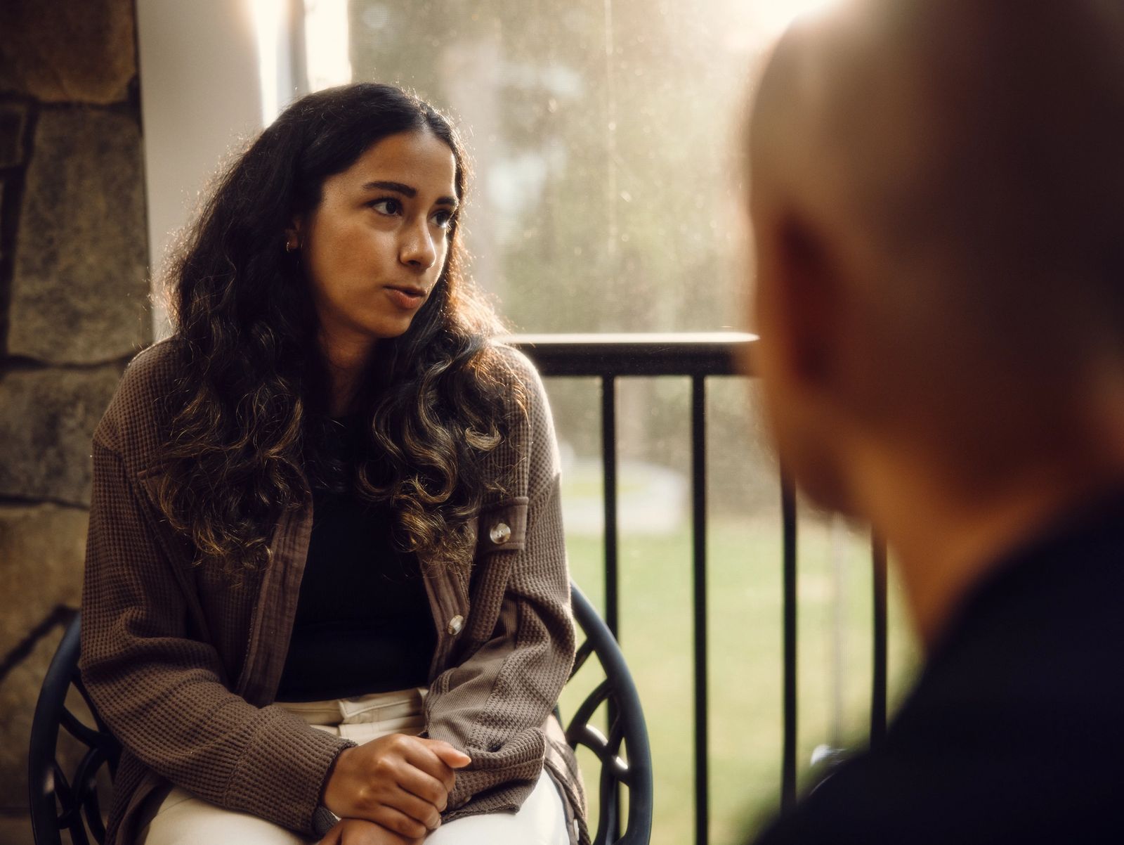 A young woman sits listening intently during a conversation with an older person on a porch.